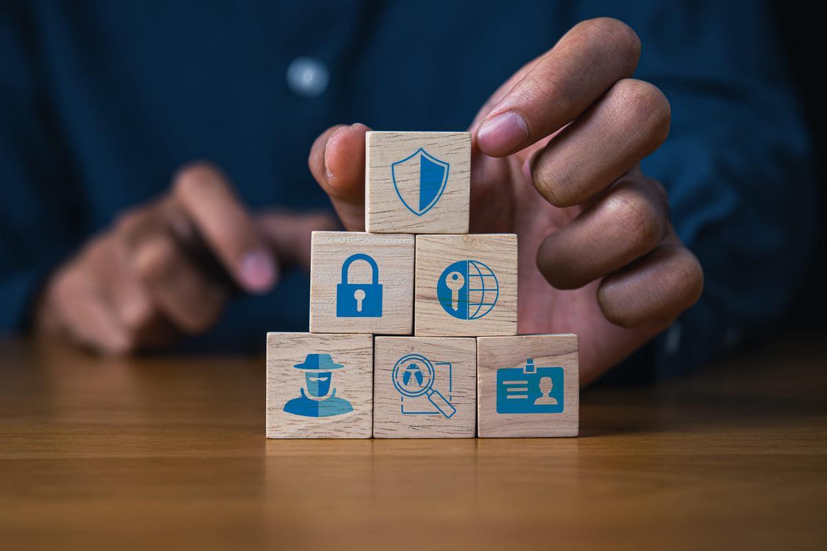 Hands stacking wooden blocks with security and identity icons, representing layered cyber insurance controls