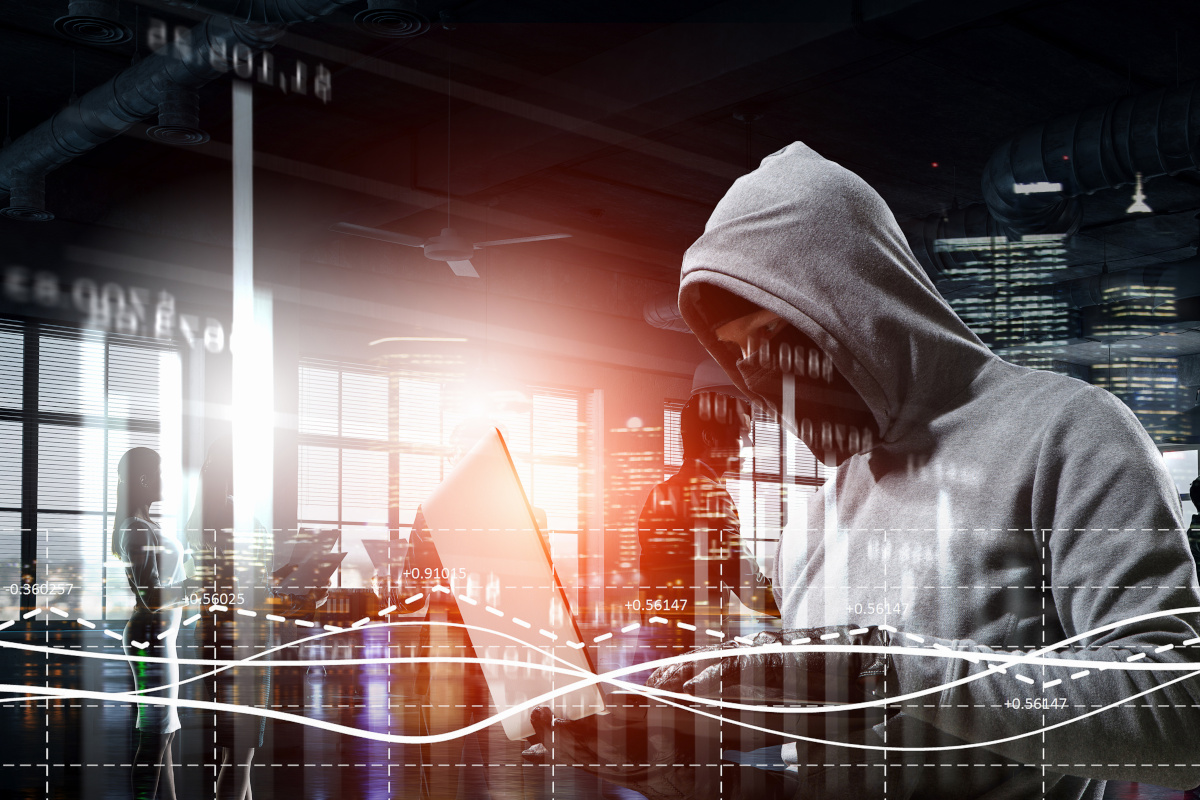 A person in a hoodie with a mask and gloves using a laptop to illustrate cyber security risks