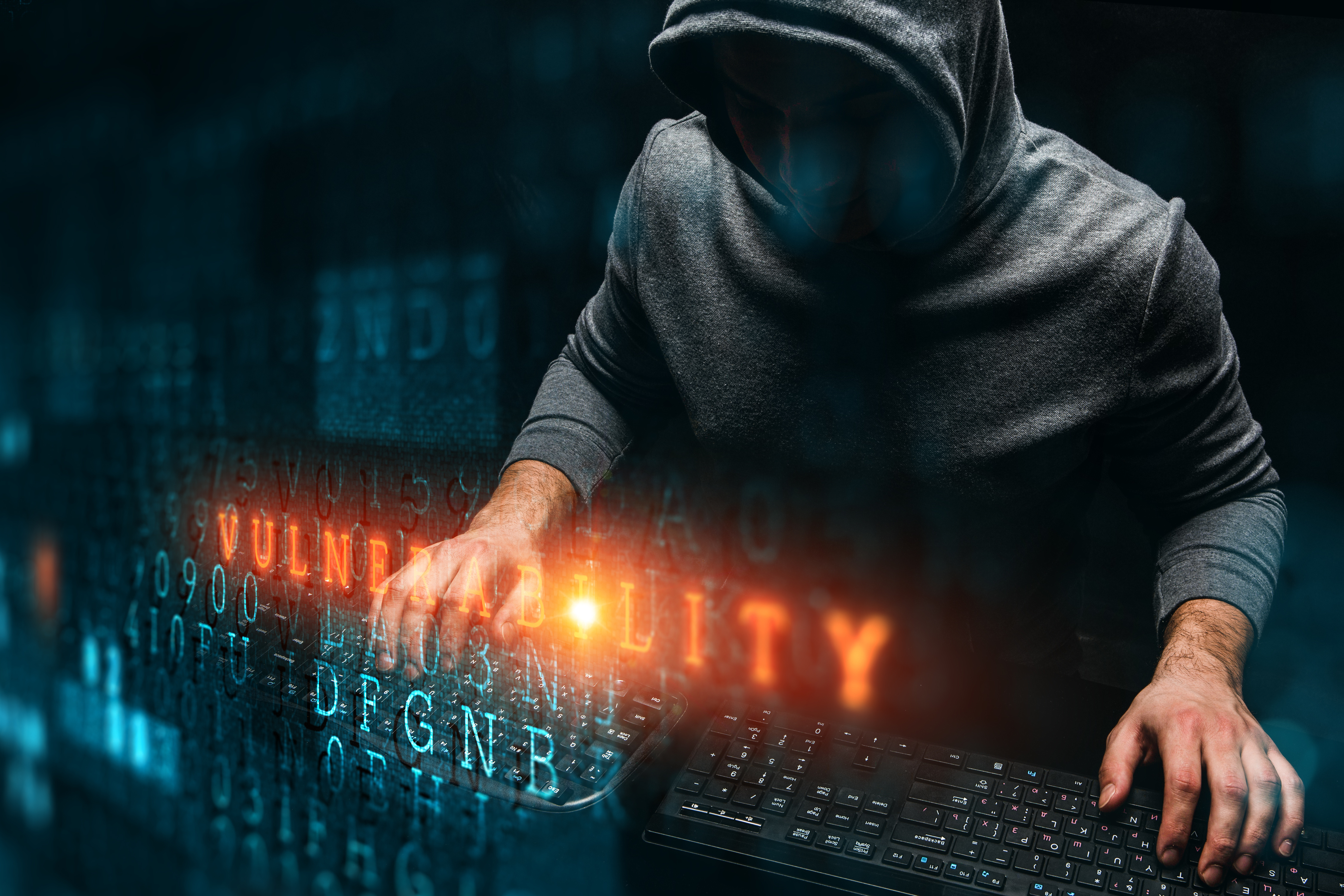 The word 'vulnerability' overlaid on a hacker typing on two keyboards