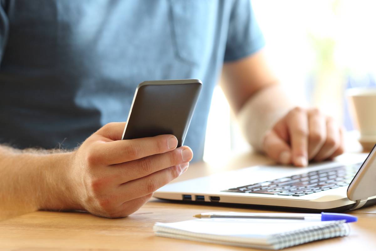 A man using a smart phone and a laptop while working at home