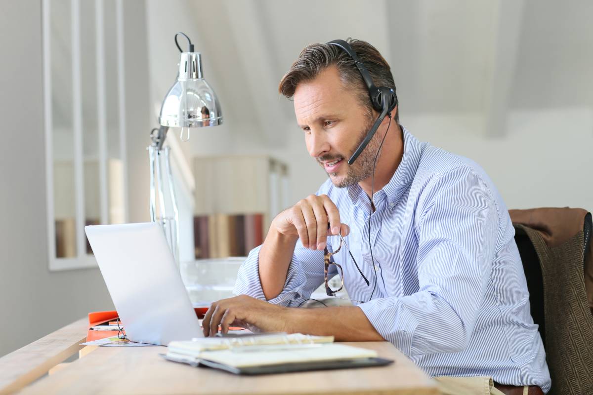 A man working from using using a laptop and a headset
